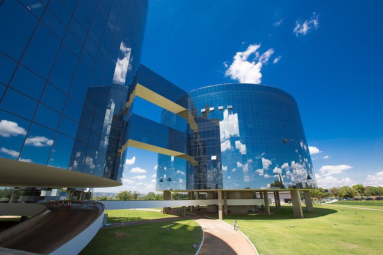 Foto dos prédios da Procuradoria-Geral da República em Brasília. Os prédios são espelhados. É um dia de Sol com poucas nuvens e é possível ver as nuvens refletidas no prédio espelhado.