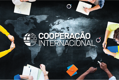 Vista superior de pessoas reunidas em volta de uma mesa com o mapa-múndi impresso e o texto "COOPERAÇÃO INTERNACIONAL" ao centro, acompanhado pelo ícone de um globo.