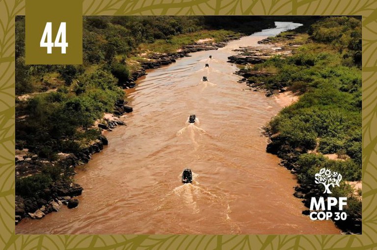 Imagem aérea de um rio cercado por vegetação. Há barcos no leito do rio.