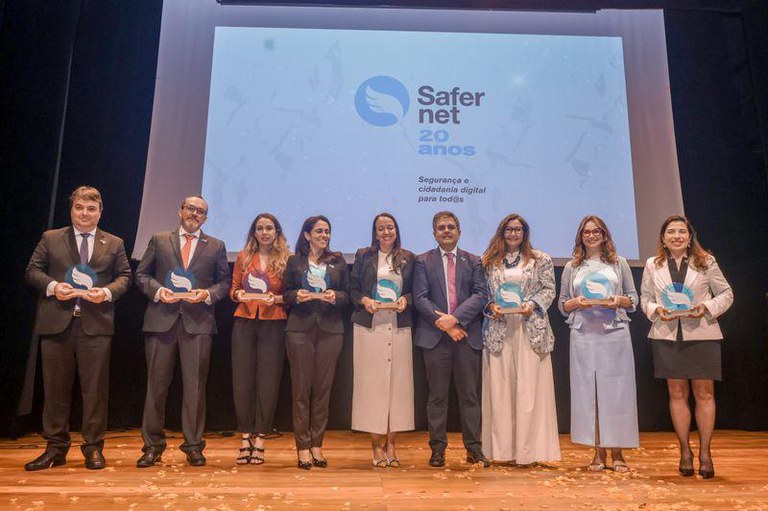foto dos participantes enfileirados lado a lado no palco do evento com um telão atrás onde se lê Safernet 20 anos segurança e cidadania digital para todos