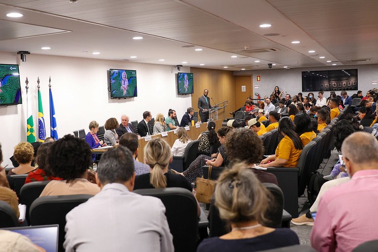 Foto de auditório lotado com mesa de debatedores ao fundo