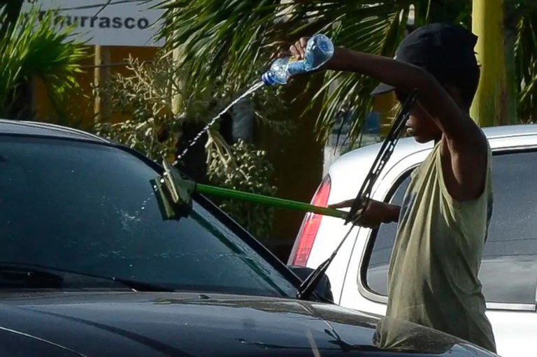 Imagem de uma criança limpando o para-brisa de um carro