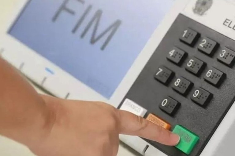 Imagem de uma mão usando a urna eletrônica de votação