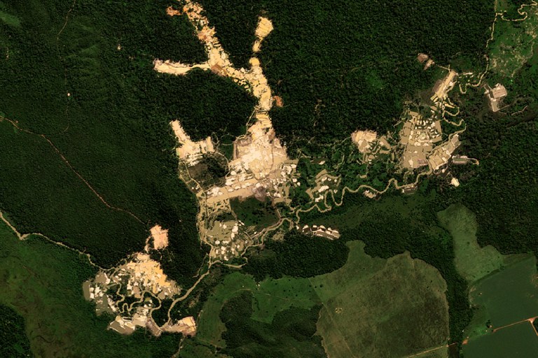 Imagem de satélite mostra área de garimpo aberta em meio à floresta, com clareiras extensas, vias e vegetação ao redor.