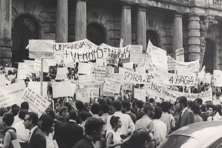Foto de Manifestação estudantil contra a Ditadura Militar, sem data. A foto é do Arquivo Nacional. Fundo Correio da Manhã (BR_RJANRIO_PH_0_FOT_00229_0297). É possível ver estudantes com cartazes e faixas. Atrás, há um prédio.