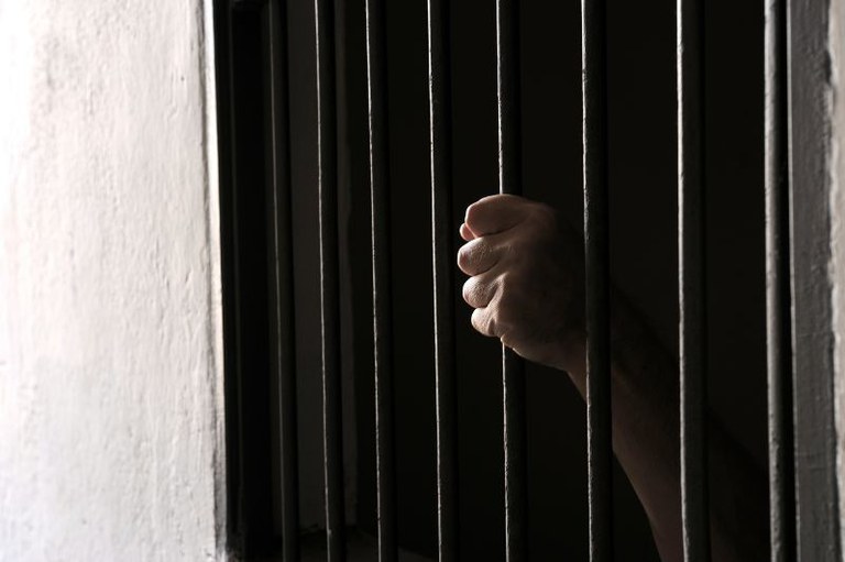 Foto em detalhe de um preso segurando a cela da prisão