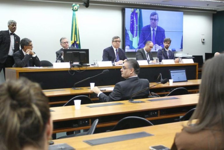 Foto da Comissão de Minas e Energia da Câmara dos Deputados que discutia o tema "Leilão de reserva de capacidade no setor elétrico brasileiro". Mais à esquerda na foto, é possível ver sentado à mesa o subprocurador-geral da República e coordenador da 3ª CCR (Consumidor e Ordem Econômica) Luiz Augusto Santos Lima. Ele está ladeado pelo presidente da comissão e convidados. Em primeiro plano, é possível ver deputados e a plateia de costas para a foto.