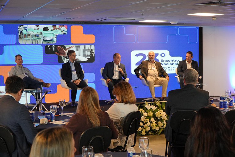 Imagem da mesa de abertura do 23º Encontro Nacional da Câmara de Combate à Corrupção, com os palestrantes sentados em cadeiras no palco e os participantes no auditório.