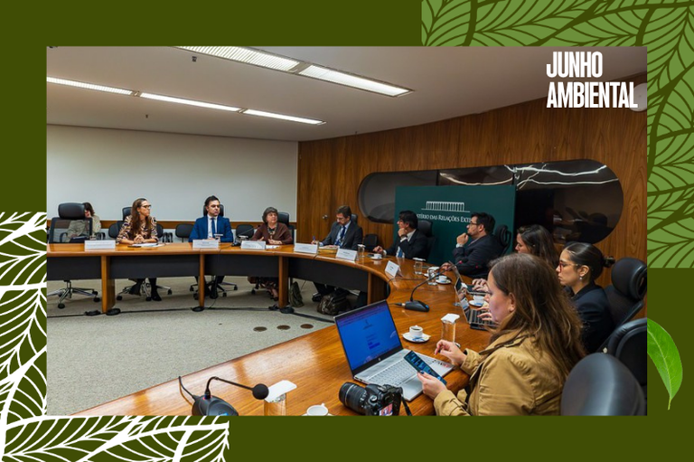 Reunião formal com várias pessoas sentadas ao redor de uma grande mesa semicircular de madeira. Ao fundo, destaca-se um painel verde com a inscrição "Ministério das Relações Exteriores".