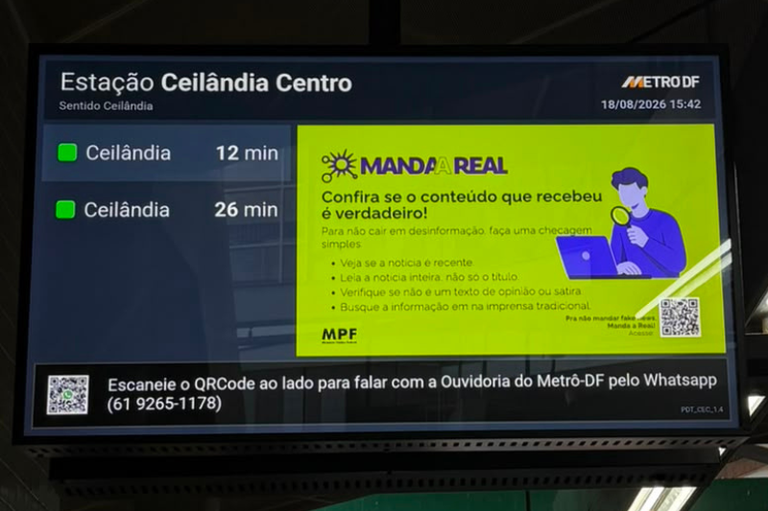 Fotografia de um painel eletrônico na Estação Ceilândia Centro do Metrô-DF, no sentido Ceilândia, registrado em 18 de agosto de 2026, às 15h42. À esquerda, o painel informa a chegada dos próximos trens, em 12 e 26 minutos. À direita, há uma peça do projeto Manda a Real, do MPF, com fundo verde, o desenho de uma pessoa usando computador e lupa e a mensagem: “Confira se o conteúdo que recebeu é verdadeiro! Para não cair em desinformação, faça uma checagem simples”, seguida das orientações “Veja se a notícia é recente”, “Leia a notícia inteira, não só o título”, “Verifique se não é um texto de opinião ou sátira” e “Busque a informação em um meio de imprensa tradicional”. A peça também apresenta um QR Code para acessar o projeto Manda a Real e o logotipo do MPF.  Na parte inferior do painel, há outro QR Code e a mensagem: “Escaneie o QRCode ao lado para falar com a Ouvidoria do Metrô-DF pelo WhatsApp (61) 9265-1178”.