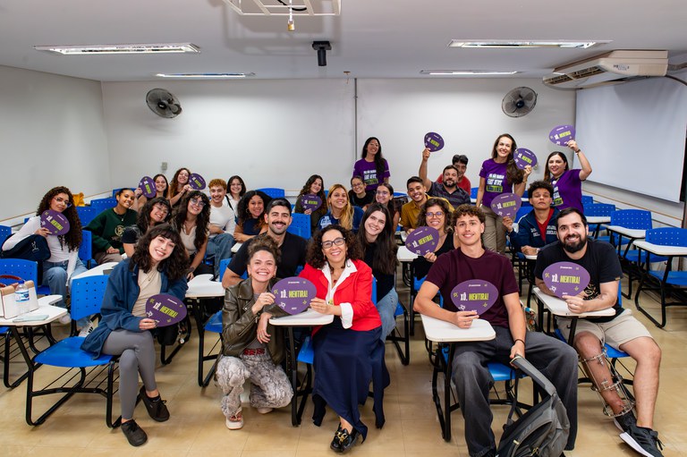 Em uma sala de aula, alunos estão sentados em cadeiras e levantam ventarolas do projeto de combate à desinformação, Manda a Real.