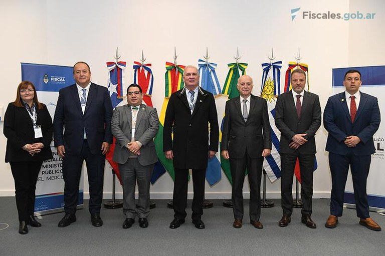 Imagem mostra sete pessoas em pé em frente a bandeiras dos países do Mercosul.