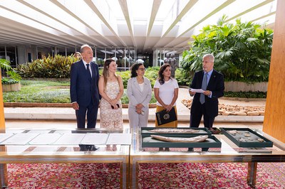 Foto da cerimônia de repatriação dos fósseis com o material em primeiro plano e as autoridades atrás da mesa discursando de pé