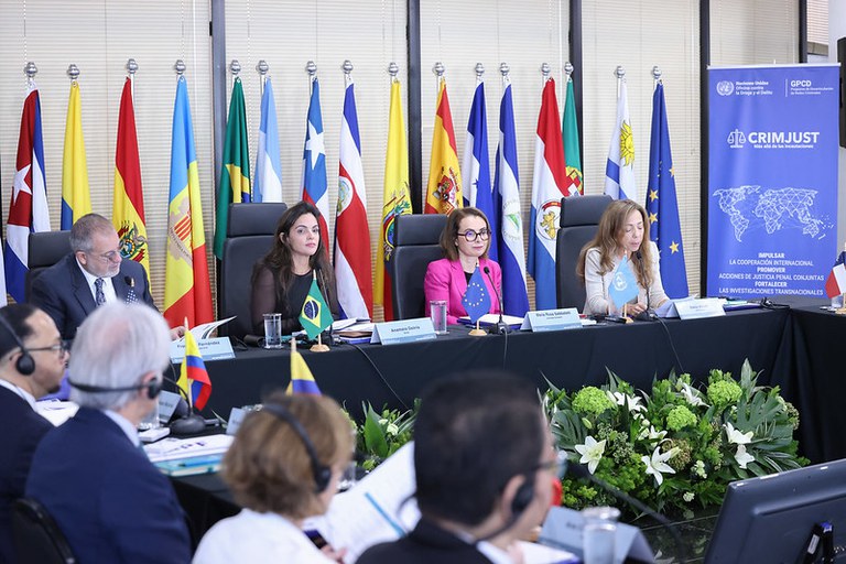 Imagem da reunião dos procuradores ibero-americanos com todos sentados em uma mesa em formato de U com as bandeiras ao fundo