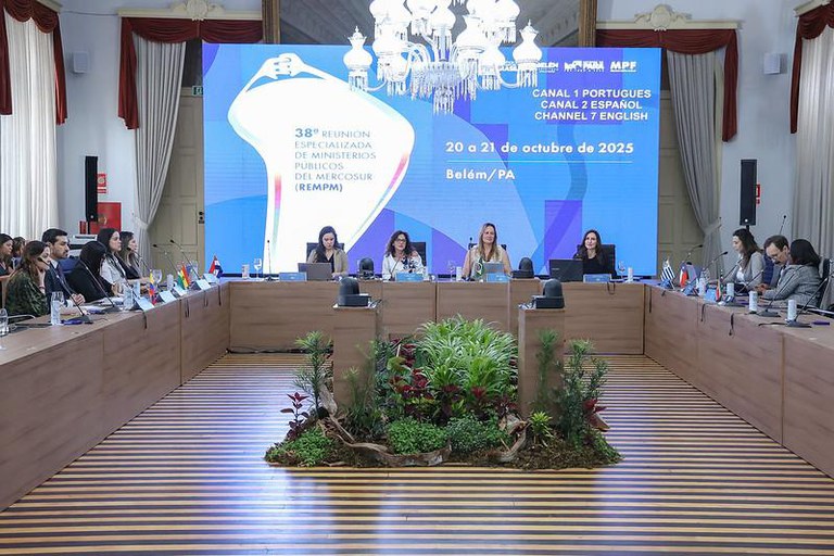 Foto da 38º Reunião Especializada de Ministérios Públicos do Mercosul - REMPM. Um auditório com uma mesa em U. É possível ver 4 pessoas centradas em cada um das bancadas que formam o U. Atrás da base do U, há um telão.