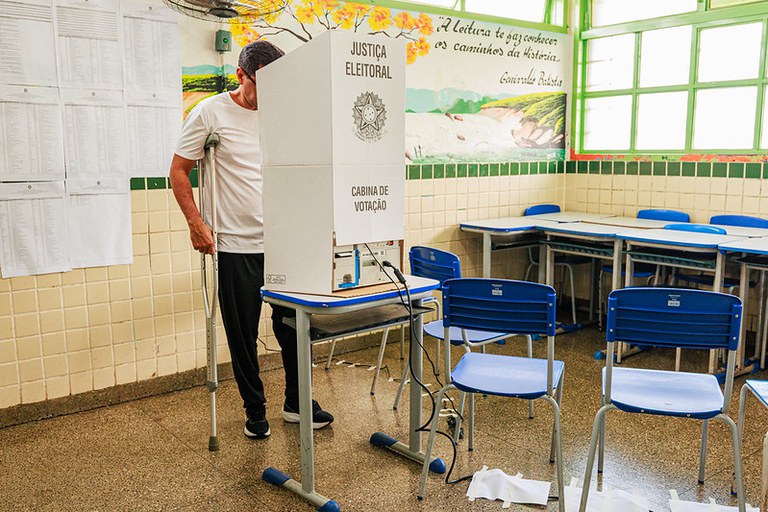 Homem de muleta que usa camisa branca e calça escura voto em cabine de votação no dia 4 de outubro de 2026 em uma escola do Distrito Federal.