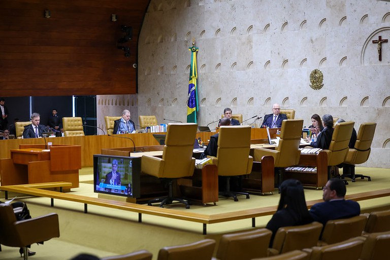 Fotografia em plano geral do plenário do Supremo Tribunal Federal (STF) durante sessão de julgamento de 24 de setembro. Em primeiro plano, de costas para a câmera, veem-se pessoas na plateia sentadas em poltronas de couro bege.

No centro do ambiente, ministros e integrantes da corte estão dispostos em uma bancada. Eles usam togas pretas sobre trajes formais. Ao fundo, a parede é revestida com placas de mármore, com o Brasão da República em relevo e um crucifixo de madeira.