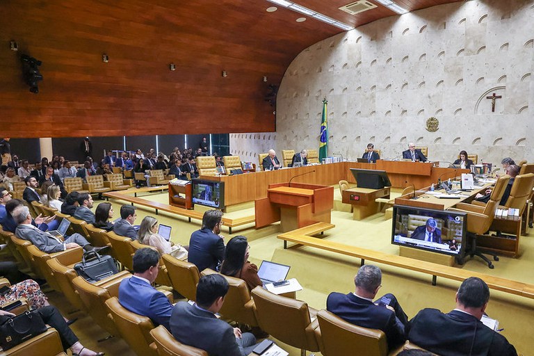 Foto mostra sessão plenária do STF, com ministros dispostos em seus lugares. A foto foi feita do ponto de vista dos ouvintes da sessão