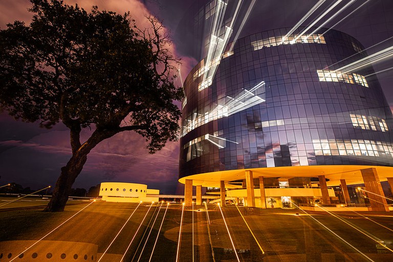 Prédio da PGR. Na foto feita ao entardecer, as luzes das salas saem dos vidros espelhados. A iluminação alaranjada do prédio também parecem fazer riscos a grama. Trata-se de técnica conhecida como "light paint".