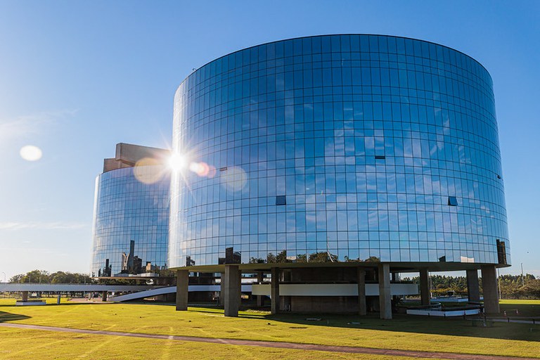 Foto do prédios sede da PGR em Brasília. Os prédios espelhados refletem o Sol. O céu está azul.