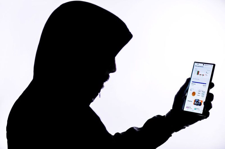 Homem encapuzado com celular na mão.