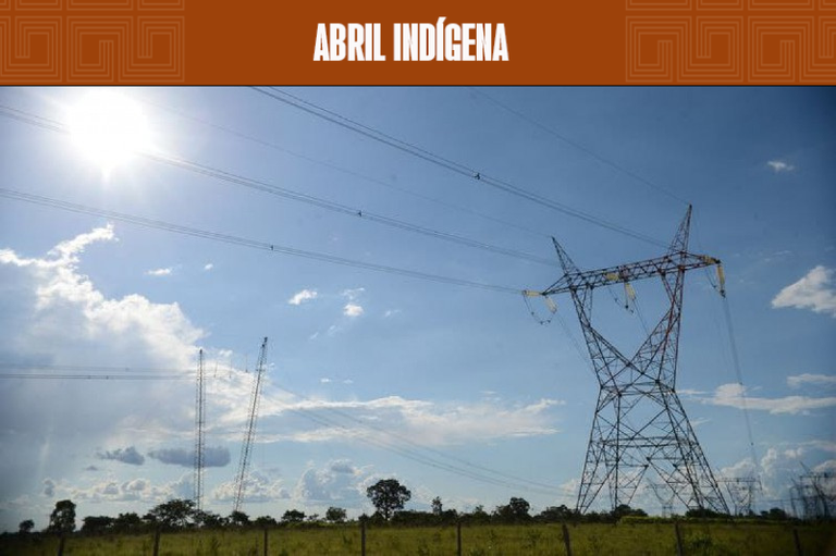 Foto mostra uma torre de transmissão de energia em uma área verde