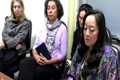 Foto mostra quatro mulheres sentadas próximas numa sala de paredes claras.