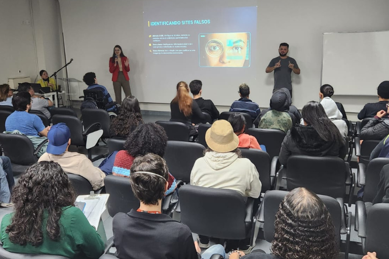 Foto mostra apresentação do projeto MPF pela Educação Social num auditório, com uma mulher de cabelos pretos e óculos apresentando informações numa projeção.