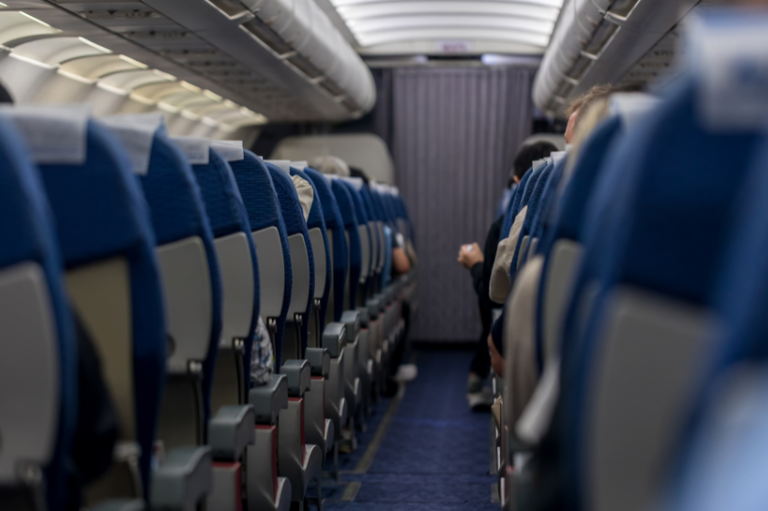 Foto interna tirada do fundo de um avião, com o corredor no meio e várias fileiras de assentos