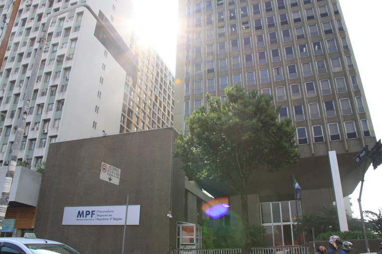 Foto mostra o prédio cinza da Procuradoria Regional da República da 3ª Região, em contraluz, com o sol aparecendo ao fundo.