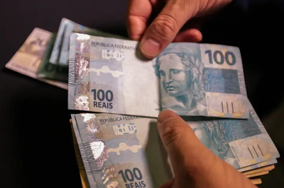 Foto mostra uma pessoa contando notas de R$ 100