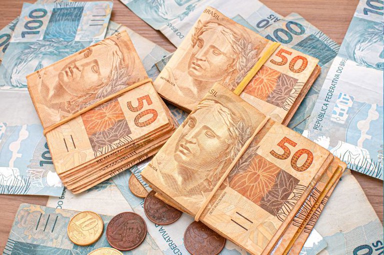 foto mostra cédulas de cem e cinquenta reais e algumas moedas