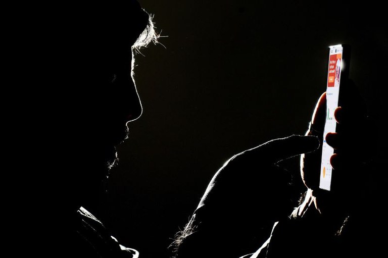 Imagem escura de um homem mexendo no celular