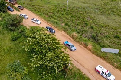 Foto aérea de várias caminhonetes de órgãos de segurança pública do Pará em estrada de terra rodeada por árvores e gramado.

