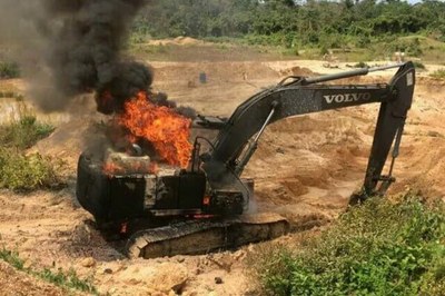 Máquina escavadeira em chamas em meio a areia e floresta.