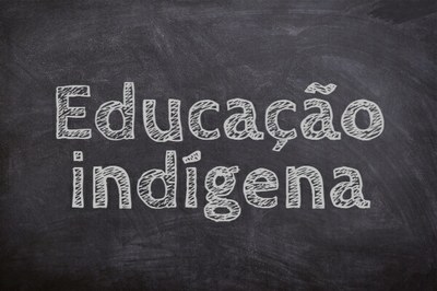 Texto "Educação indígena" com tipografia que imita letras pintadas a giz. Ao fundo, imagem que imita quadro-negro.
