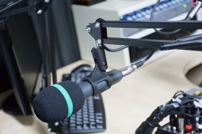 Imagem de um estúdio de rádio, com microfone, teclado de computador, mesa de som, fios e cabos.