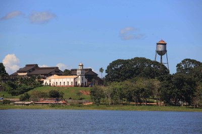 Foto de parte do distrito de Fordlândia, em Aveiro, no Pará, vista do rio Tapajós. Há uma igreja, vários galpões, casas e uma caixa de água feita em ferro. Todas essas instalações têm arquitetura estilo americana da década de 1930.