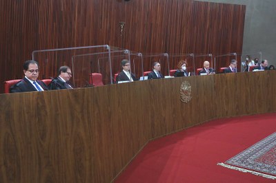 Foto de oito ministros e uma ministra do TSE reunidos em salão do tribunal. A bancada é de madeira, e a parede ao fundo também. Na bancada há um brasão nacional, e ao fundo alguns funcionários do tribunal. O chão é de carpete vermelho.