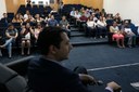 O procurador regional dos Direitos do Cidadão, Guilherme Ferraz, aparece de perfil em primeiro plano. O foco da imagem está no público de cerca de 35 pessoas que está sentado e assiste o painel de apresentação.  
