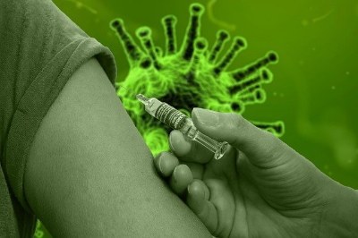 Foto em tons esverdeados de um braço de pessoa com vacina sendo aplicada, com ilustração do novo coronavírus ao fundo.