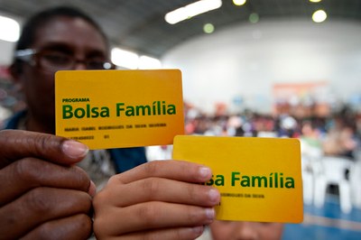 A imagem mostra duas pessoas segurando o cartão do Bolsa Família.