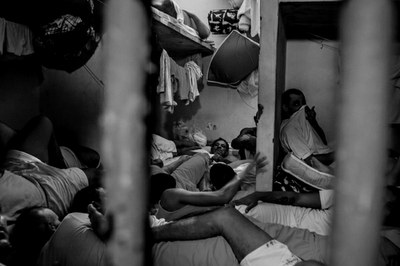 Imagem do interior de uma cela carcerária com presos deitados no chão
