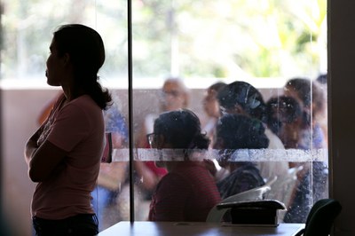 A imagem mostra um grupo de venezuelanos em uma sala de espera aguardando atendimento.