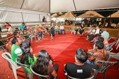 Foto de indígenas sentados em cadeiras dispostas em círculo, reunidos com membro do MPF, em tenda no Acampamento Terra Livre