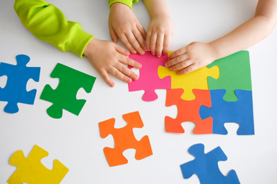 Foto de crianças de montando um quebra-cabeças colorido. O quebra-cabeças colorido é o símbolo do autismo