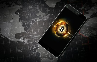 #Pracegover Imagem de uma moeda amarela brilhante em um celular representando criptomoedas. O celular está sobre um mapa mundi  