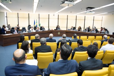 Foto da mesa principal da reunião do Conselho, e parte do público presente.