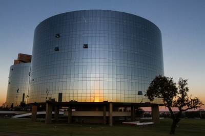 Foto dos prédios da PGR que recebem a luz do sol poente. À direita tem uma árvore típica do Cerrado.