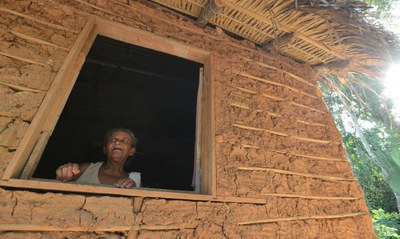 #pracegover: foto de uma senhora quilombola à janela de uma casa de pau a pique